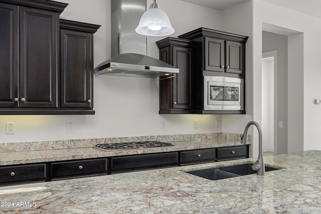 kitchen with wall chimney range hood, decorative light fixtures, sink, and appliances with stainless steel finishes