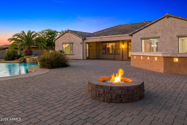 pool at dusk with an outdoor fire pit and a patio