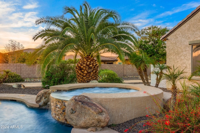 pool at dusk with an in ground hot tub and pool water feature