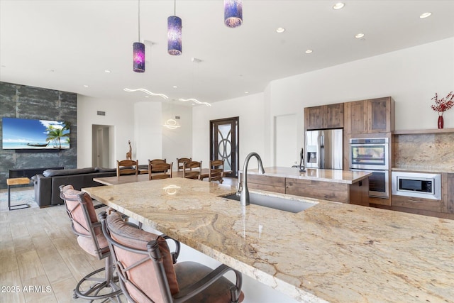 kitchen with sink, light stone counters, a large fireplace, appliances with stainless steel finishes, and pendant lighting