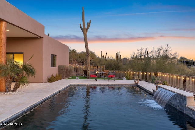 pool at dusk featuring pool water feature and a patio