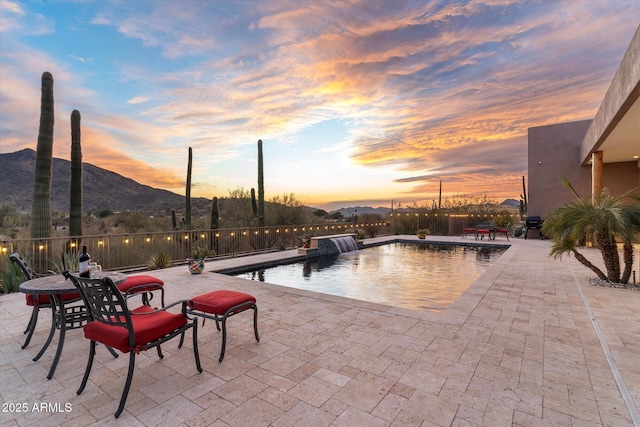 pool at dusk with a mountain view, a patio area, and pool water feature