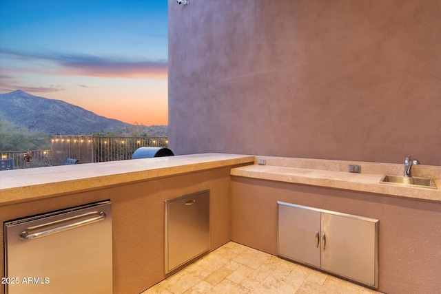 patio terrace at dusk featuring exterior kitchen, a mountain view, and sink