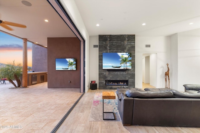 living room featuring ceiling fan, a tile fireplace, and light wood-type flooring