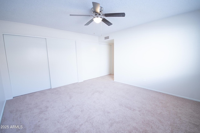 unfurnished bedroom featuring ceiling fan, light colored carpet, a closet, and a textured ceiling