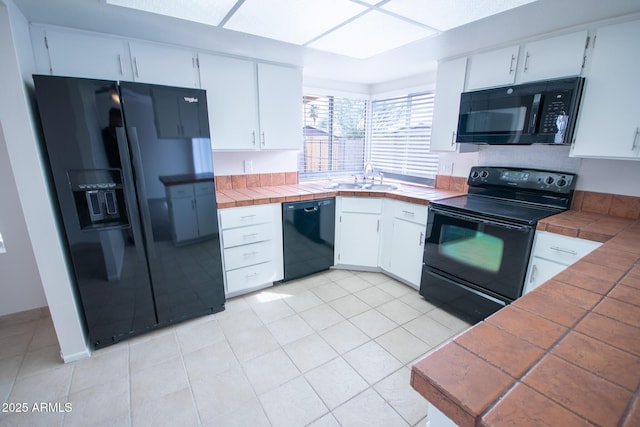 kitchen with sink, black appliances, light tile patterned floors, tile counters, and white cabinets