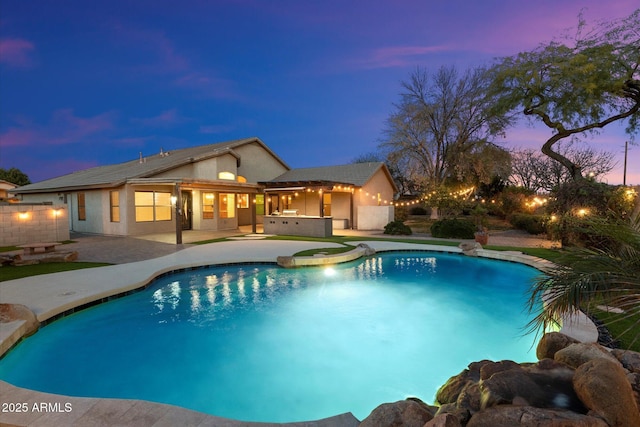 pool at dusk with an in ground hot tub and a patio