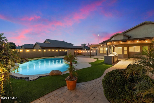 pool at dusk with a yard, a patio, and an outdoor kitchen