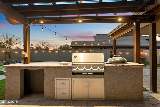 patio terrace at dusk featuring area for grilling and exterior kitchen