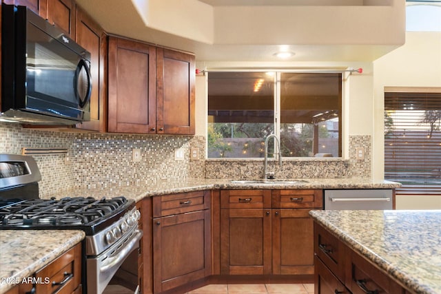 kitchen featuring sink, light tile patterned floors, backsplash, light stone counters, and stainless steel gas range oven