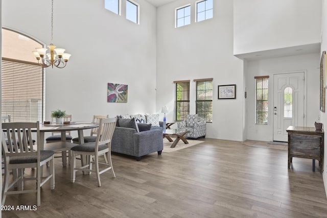 dining area with wood-type flooring, a towering ceiling, an inviting chandelier, and plenty of natural light