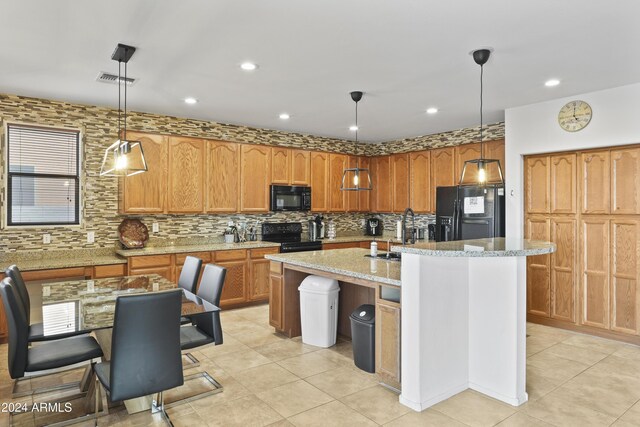 kitchen featuring black appliances, sink, light stone countertops, an island with sink, and decorative light fixtures