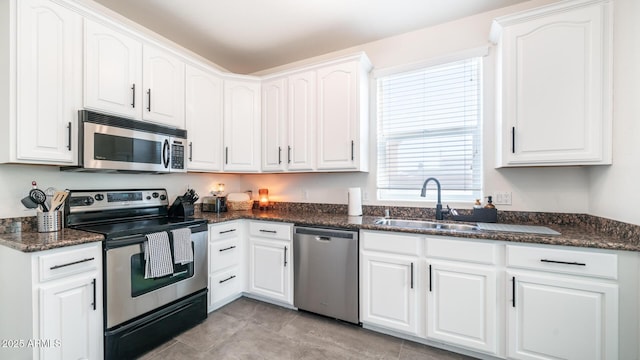 kitchen featuring sink, white cabinetry, stainless steel appliances, light tile patterned floors, and dark stone counters