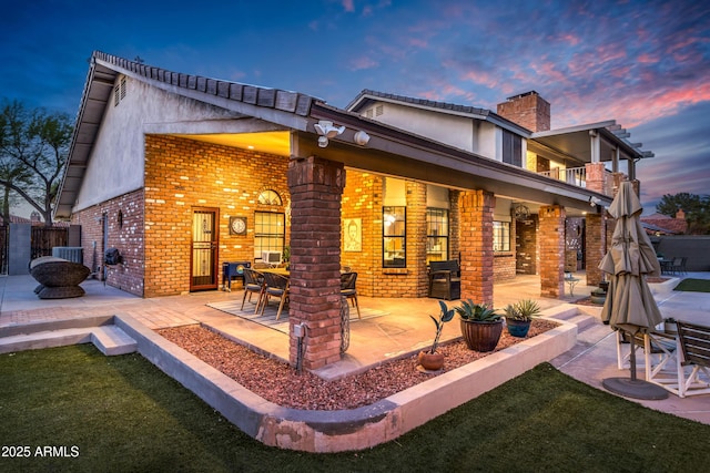 7763 W Libby St, Glendale, AZ 85308 - back of property at dusk with a balcony, a chimney, cooling unit, a patio, and brick siding