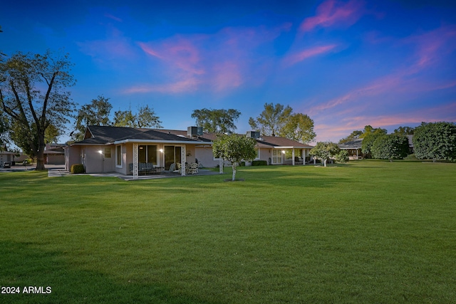 back house at dusk featuring covered porch and a lawn