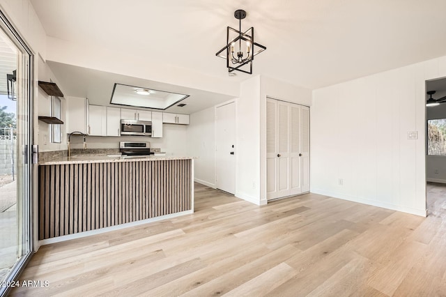 kitchen with white cabinets, kitchen peninsula, light hardwood / wood-style flooring, hanging light fixtures, and appliances with stainless steel finishes