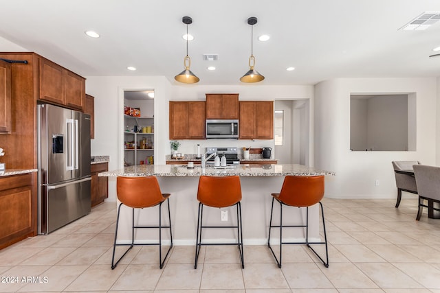 kitchen featuring an island with sink, light stone counters, decorative light fixtures, and stainless steel appliances