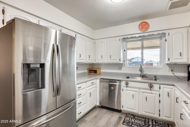 kitchen with appliances with stainless steel finishes, white cabinetry, sink, backsplash, and light wood-type flooring