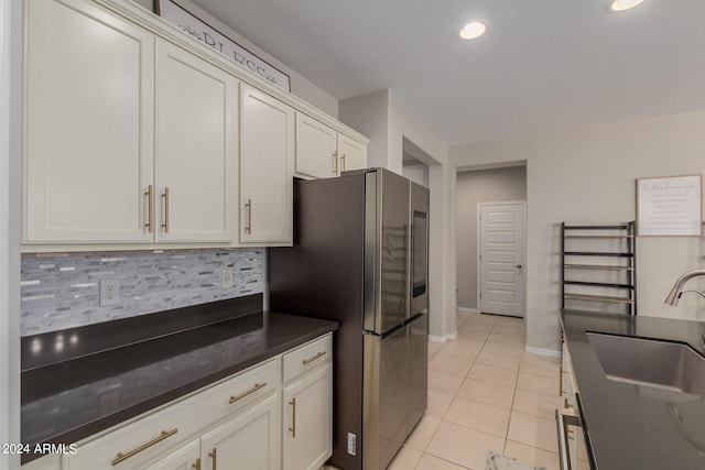 kitchen with tasteful backsplash, sink, white cabinets, stainless steel refrigerator, and light tile patterned flooring