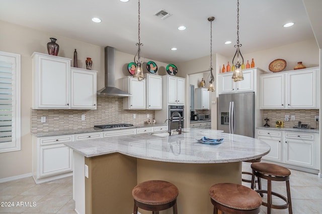 kitchen featuring a center island with sink, white cabinets, wall chimney range hood, appliances with stainless steel finishes, and a kitchen bar