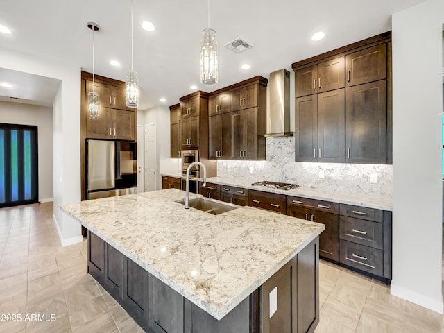 kitchen featuring sink, wall chimney exhaust hood, hanging light fixtures, a center island with sink, and appliances with stainless steel finishes