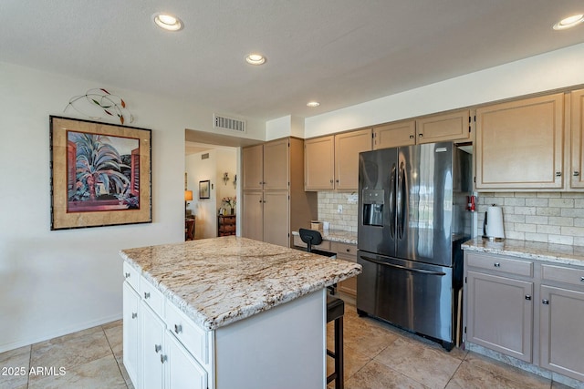 kitchen with tasteful backsplash, stainless steel fridge, a kitchen island, and light stone countertops