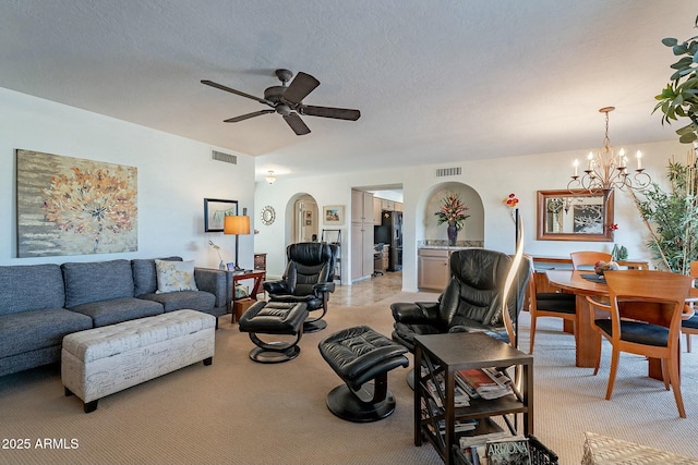 living room featuring ceiling fan with notable chandelier, light colored carpet, and a textured ceiling