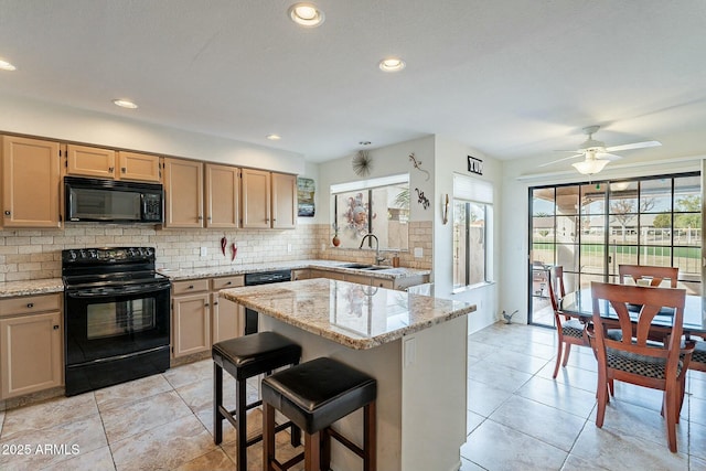 kitchen featuring light stone countertops, a kitchen breakfast bar, sink, black appliances, and a center island