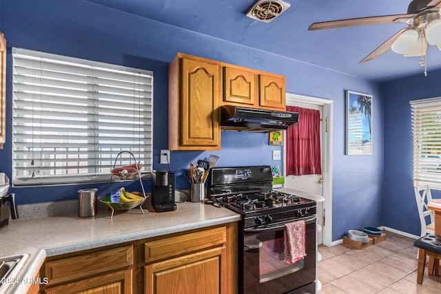 kitchen with light tile patterned floors, under cabinet range hood, a ceiling fan, black gas stove, and brown cabinetry