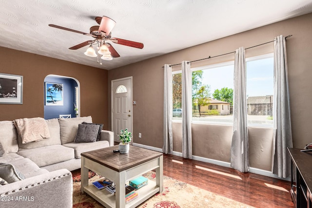 living room featuring a ceiling fan, arched walkways, baseboards, and wood finished floors