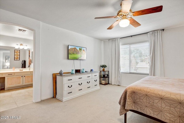 bedroom with light carpet, ensuite bath, visible vents, and arched walkways