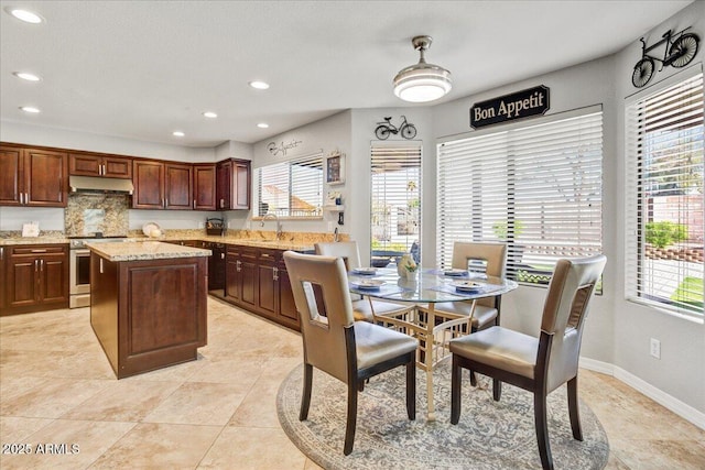 kitchen with a center island, electric range, a sink, under cabinet range hood, and baseboards