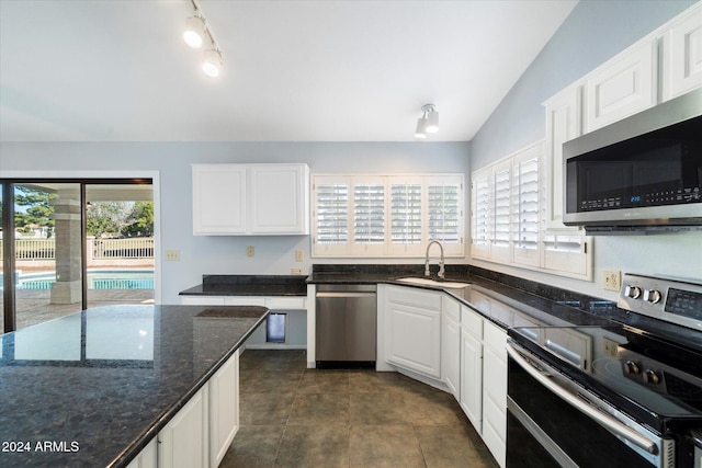 kitchen with sink, stainless steel appliances, dark stone counters, lofted ceiling, and white cabinets