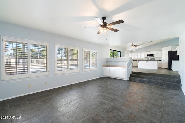 unfurnished living room featuring ceiling fan, dark tile patterned floors, and vaulted ceiling