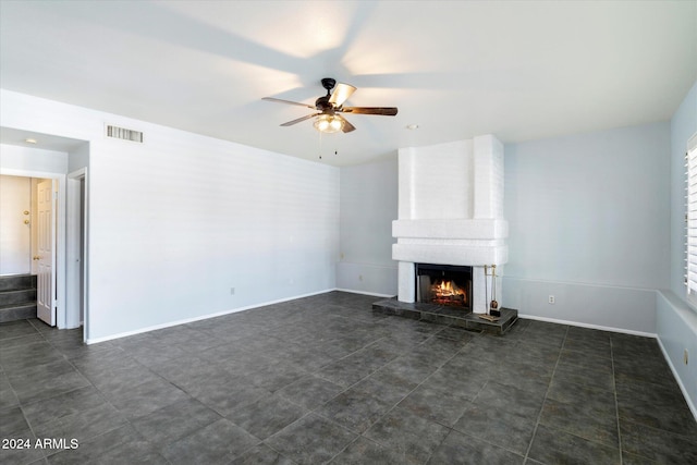 unfurnished living room with a large fireplace, dark tile patterned flooring, and ceiling fan