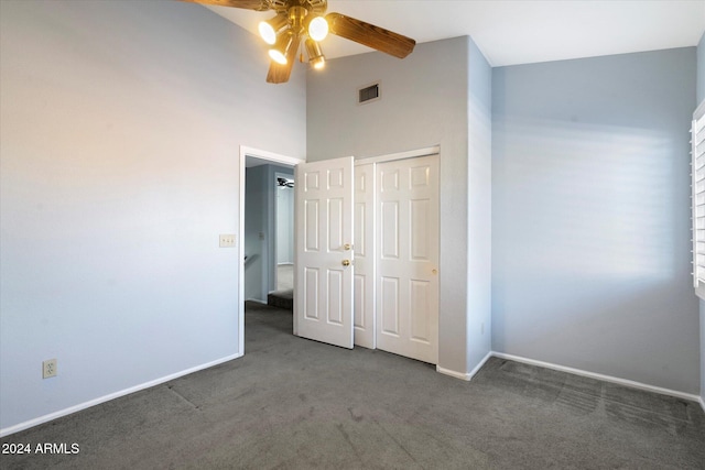 unfurnished bedroom featuring dark colored carpet, a towering ceiling, a closet, and ceiling fan