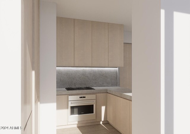 kitchen with kitchen peninsula, light brown cabinets, light wood-type flooring, black gas stovetop, and sink