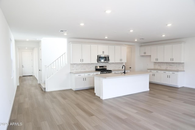 2482 W Rowel Rd, Phoenix, AZ 85085 - kitchen featuring stainless steel appliances, a sink, light wood-style floors, decorative backsplash, and a kitchen island with sink