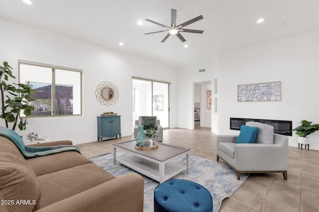 living room featuring light tile patterned floors, a glass covered fireplace, a ceiling fan, and recessed lighting