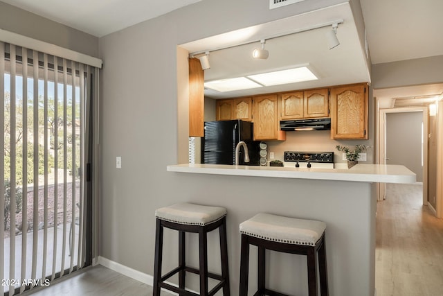 kitchen featuring a kitchen bar, black appliances, track lighting, and light hardwood / wood-style floors