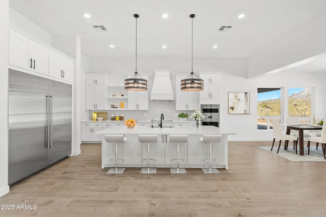 kitchen featuring backsplash, light countertops, custom range hood, appliances with stainless steel finishes, and a sink