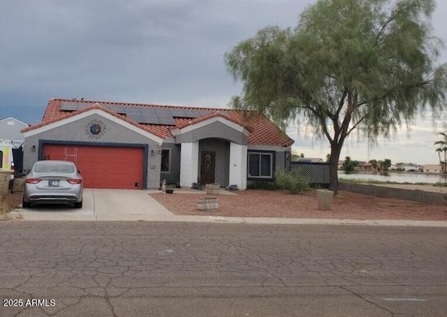 mediterranean / spanish-style house with a garage, concrete driveway, a tiled roof, roof mounted solar panels, and stucco siding