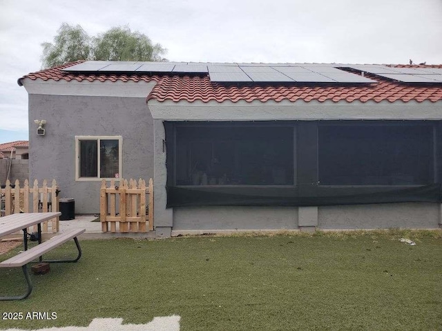 rear view of property with a tile roof, stucco siding, a lawn, a sunroom, and roof mounted solar panels