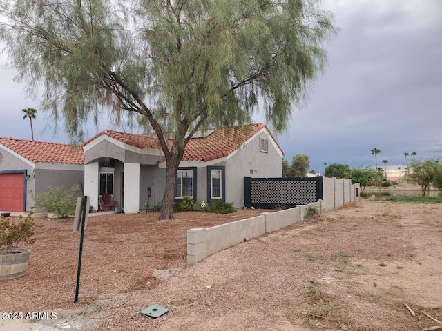 mediterranean / spanish home with a tiled roof, fence, and stucco siding