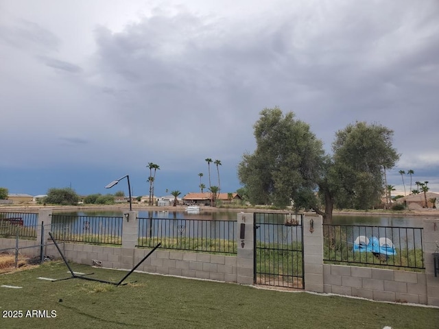 view of gate with a yard, a water view, and fence