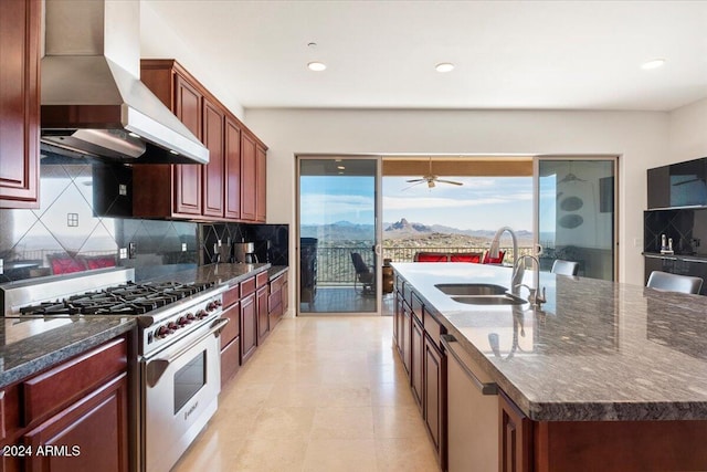 kitchen with backsplash, a center island with sink, sink, stainless steel stove, and wall chimney exhaust hood