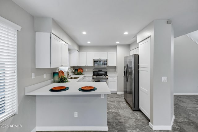 kitchen with light countertops, appliances with stainless steel finishes, a peninsula, white cabinetry, and a sink