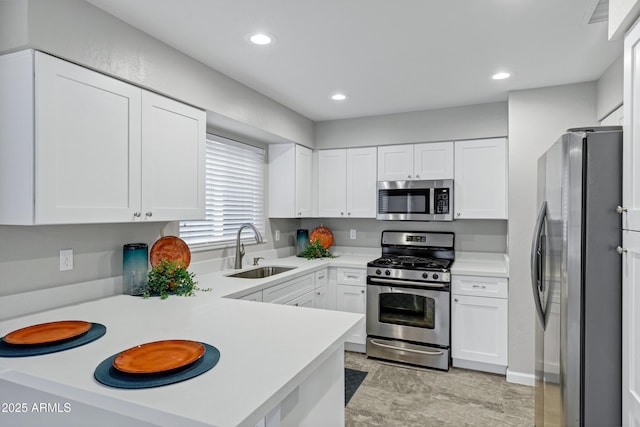 kitchen with light countertops, appliances with stainless steel finishes, a peninsula, white cabinetry, and a sink