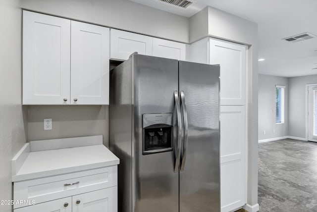 kitchen with visible vents, baseboards, light countertops, white cabinets, and stainless steel fridge