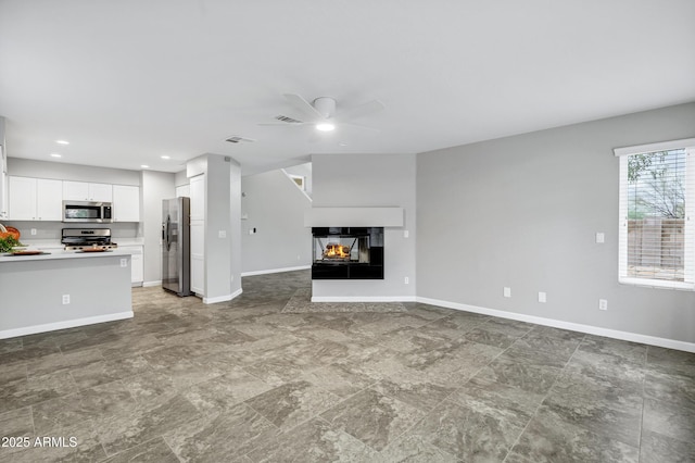 unfurnished living room featuring a ceiling fan, visible vents, a multi sided fireplace, and baseboards